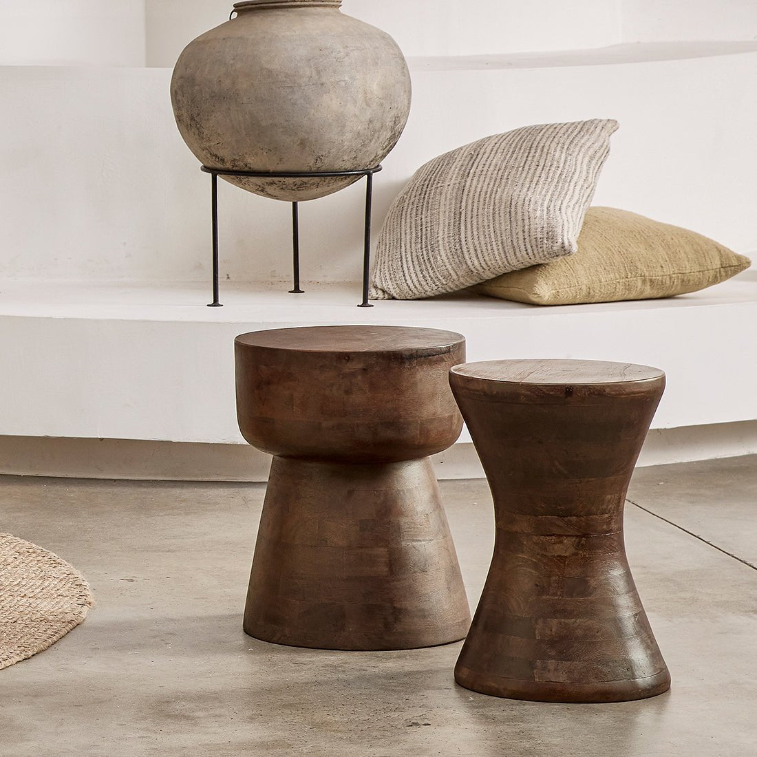 Two rustic wooden stools in a room with a vase and pillows.