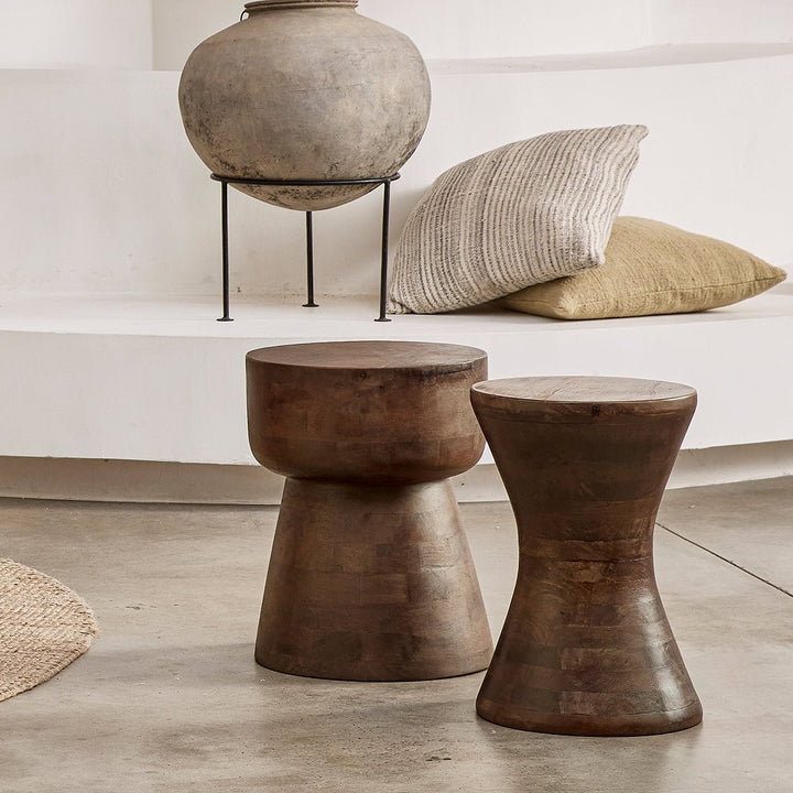 Two rustic wooden stools in a room with a vase and pillows.