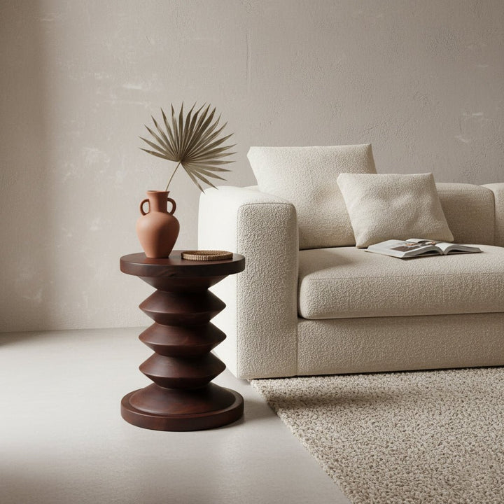 Beige sofa with decorative pillows and a wooden side table with a vase and plant in a minimalistic living room.