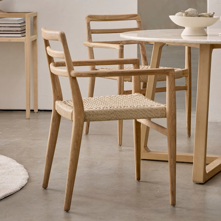 Wooden chairs with woven seats around a dining table in a minimalistic room.