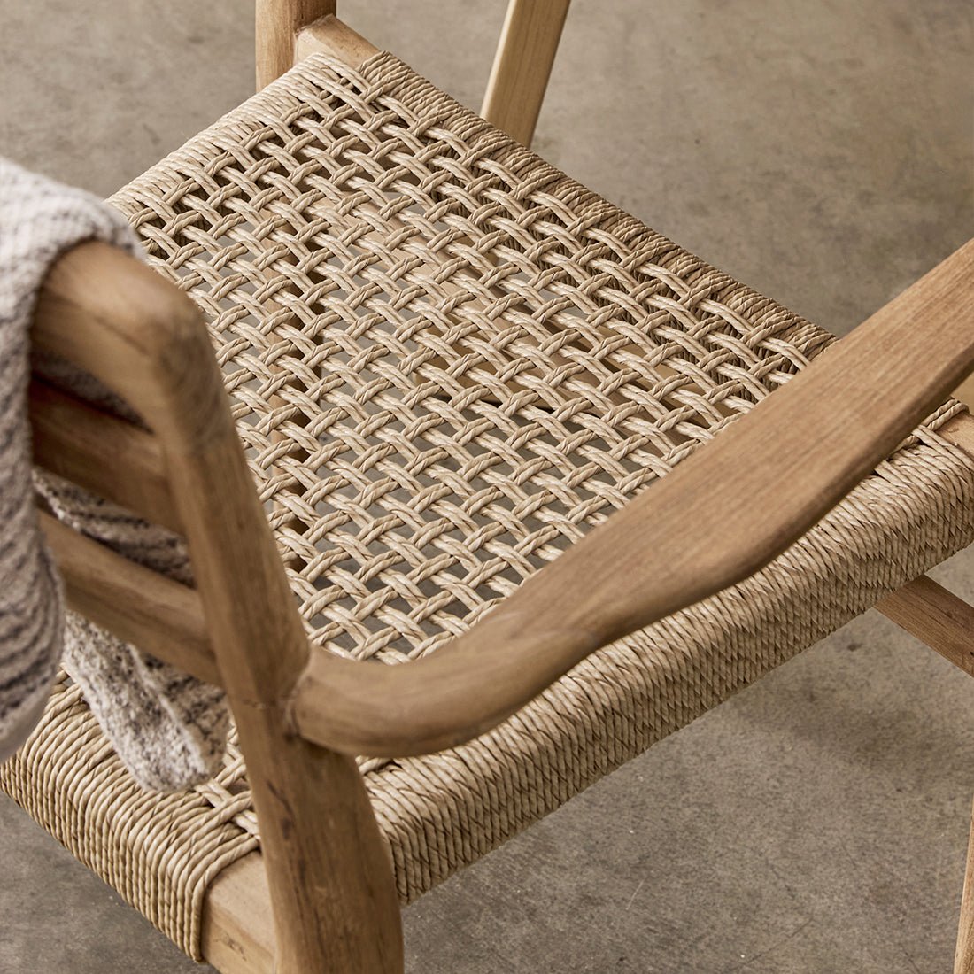 Close-up of a wooden chair with woven seat and backrest on a concrete floor.