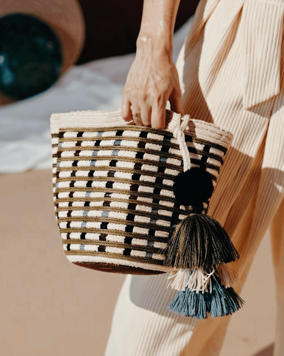 Woven handbag with tassels held by a person in a neutral setting
