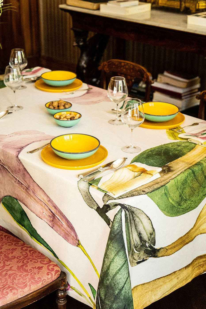 Dining table set with yellow bowls, wine glasses, and a decorative tablecloth with leaf patterns.