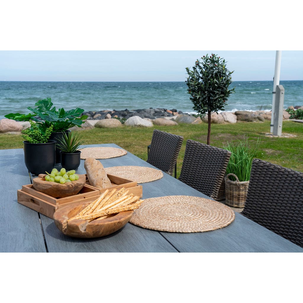 4 round braided natural jute placemats on outdoor dining table by the sea.