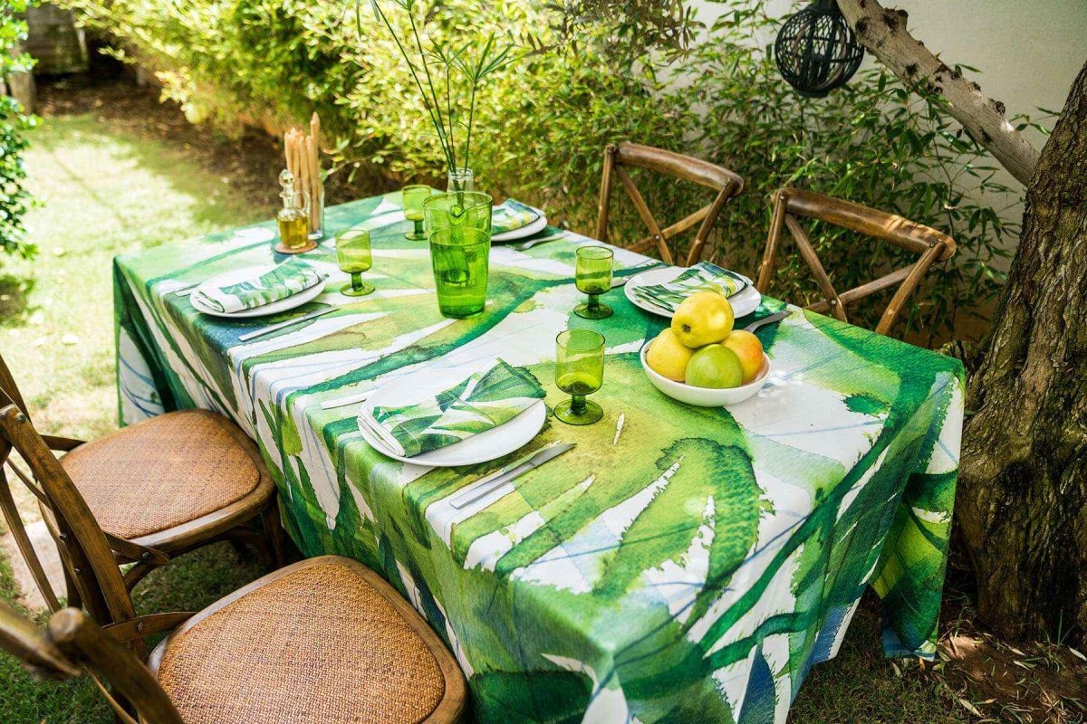 Outdoor setting with a table set for a meal on a green patterned tablecloth.