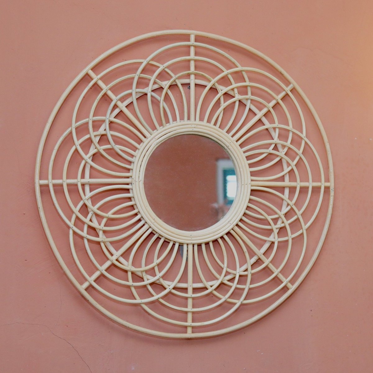 Decorative round mirror with wicker-like frame on a pink wall