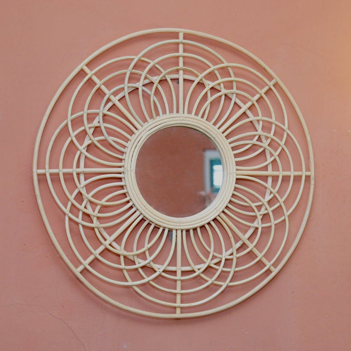 Decorative round mirror with wicker-like frame on a pink wall