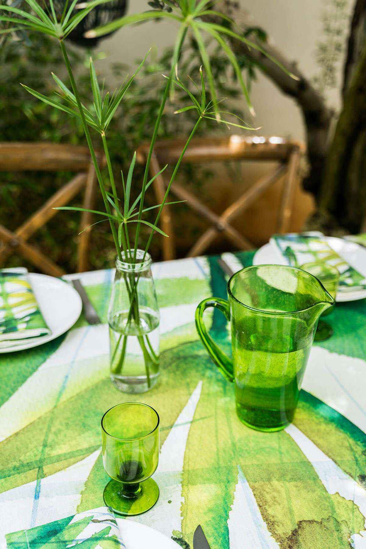 Green glass pitcher and cup on a table with a leaf-patterned tablecloth.