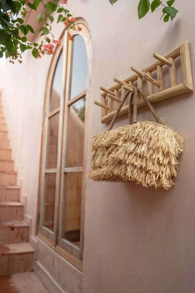 Island Coat Rack made of natural teakwood, mounted on an indoor wall, holding a decorative straw bag.