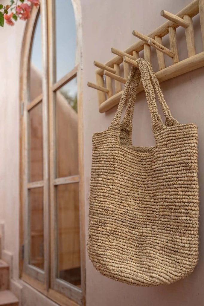 Island Coat Rack made of solid teak wood hanging on a wall, with a natural woven bag hanging from it.