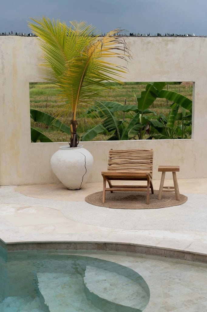 Islander Eenzit - Natural teak wood chair beside pool and plant, outdoor setting.