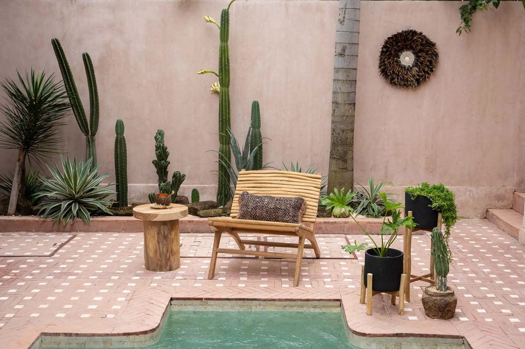 Handcrafted teak wood chair by a pool in a garden setting, featuring plants.