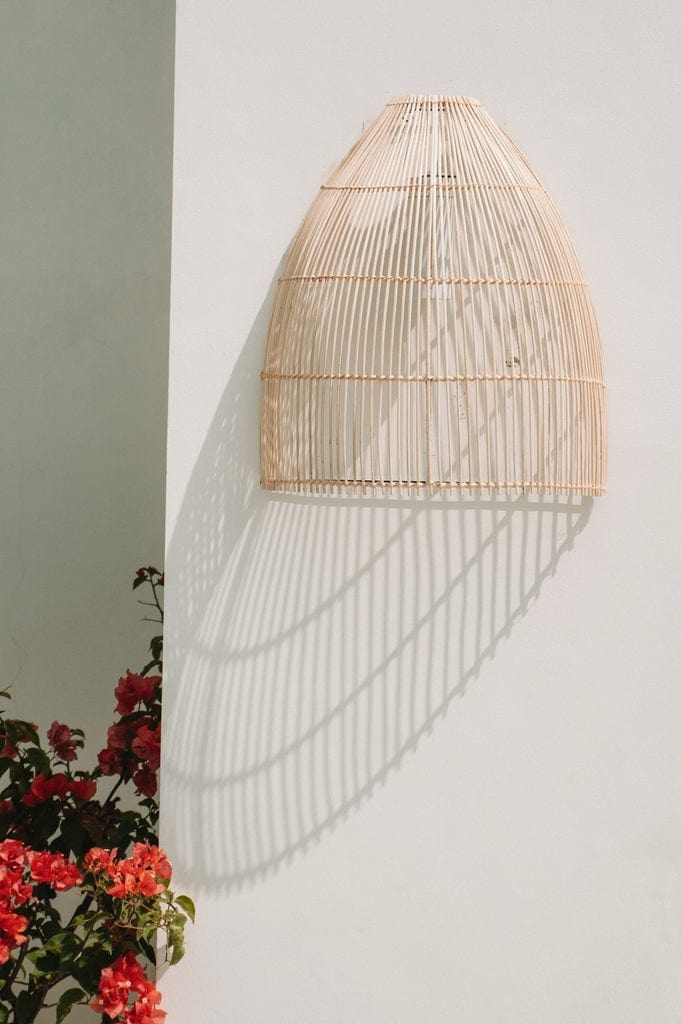 Lalo Wall Lamp - Natural rattan wall sconce on white wall with red flowers.