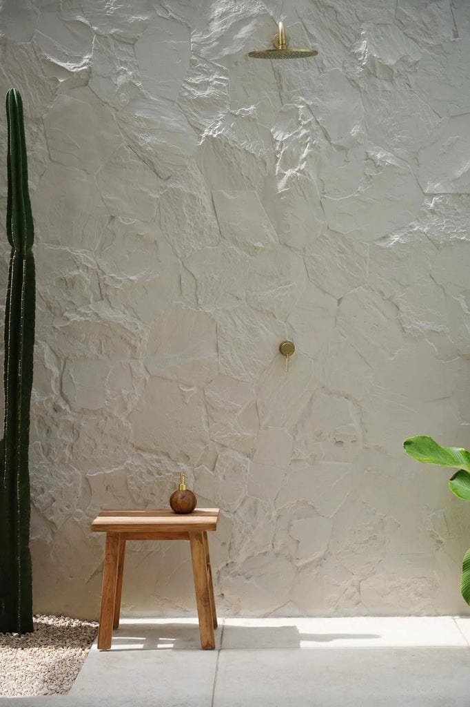 Makara Stool made from natural reclaimed teak wood, displayed against a textured wall with cactus plant.