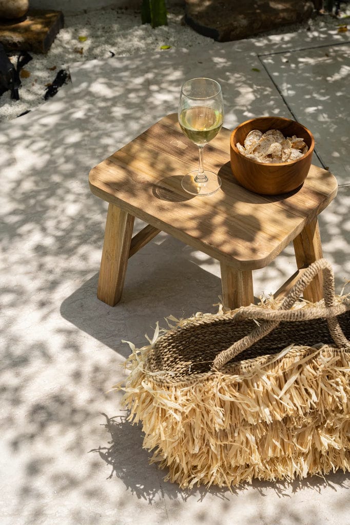 Quincy Stool made of natural reclaimed teak wood with a spacious rectangular top, suitable for indoor and covered outdoor use, shown with decor items.