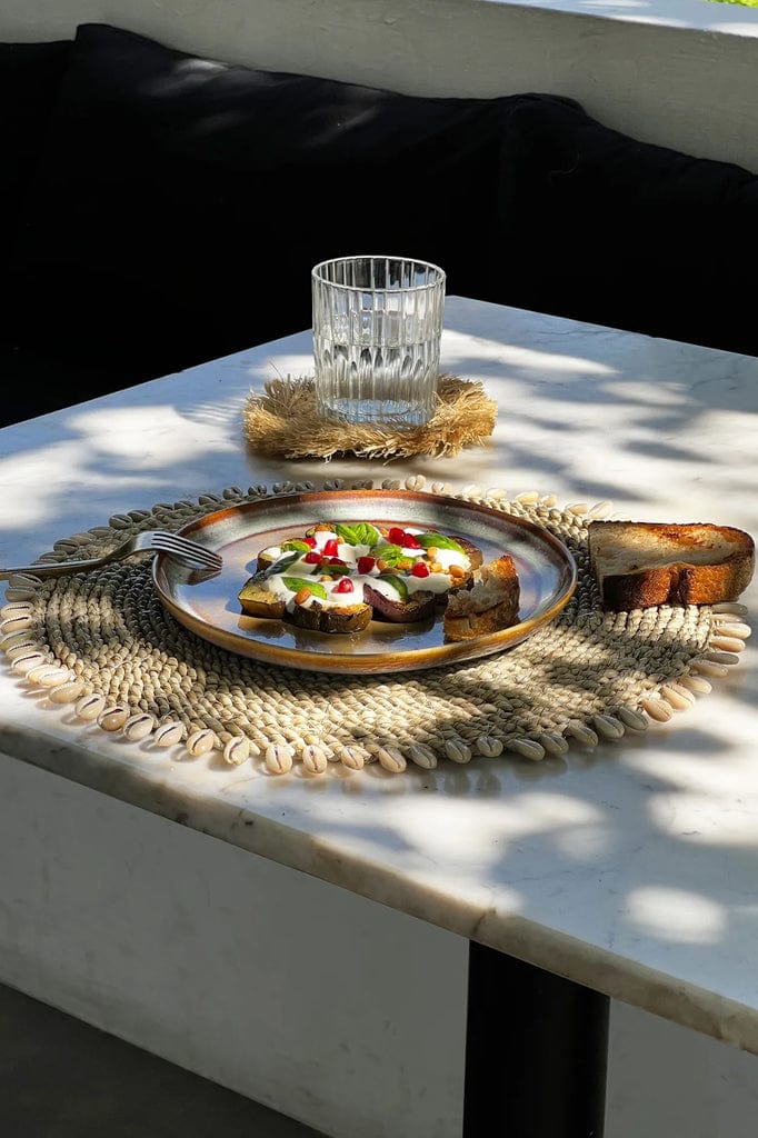 Seagrass shell placemat with cowrie shell border on dining table.