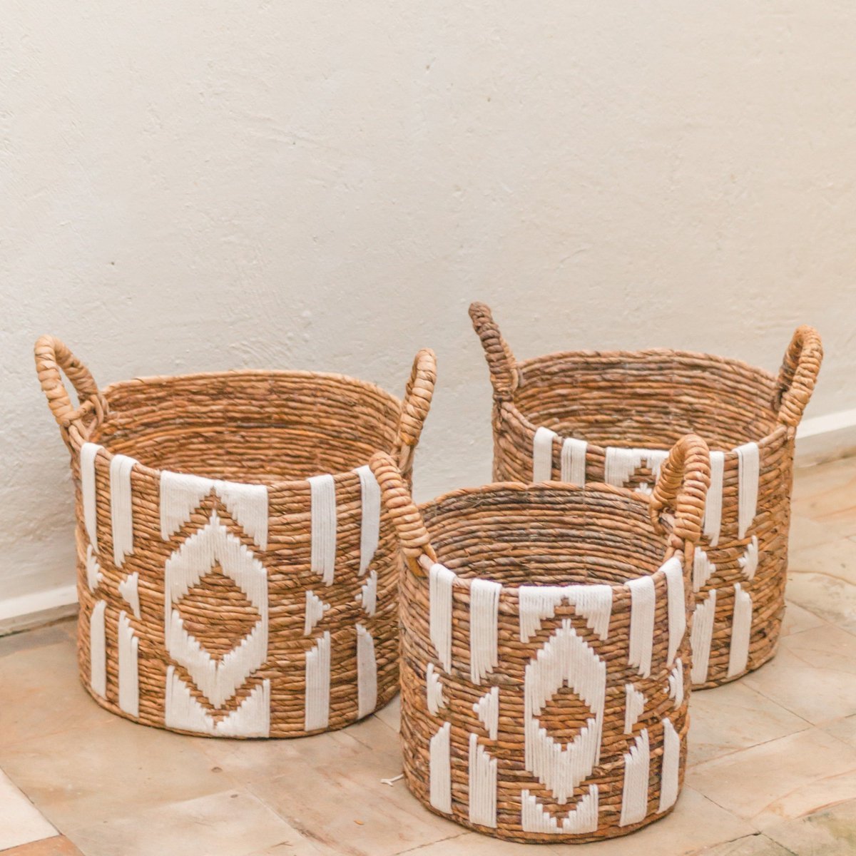Three woven baskets with geometric patterns on a light wooden floor.