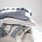 Felinia Cushion 60x40 cm Blue with tassels on top of stacked throws.