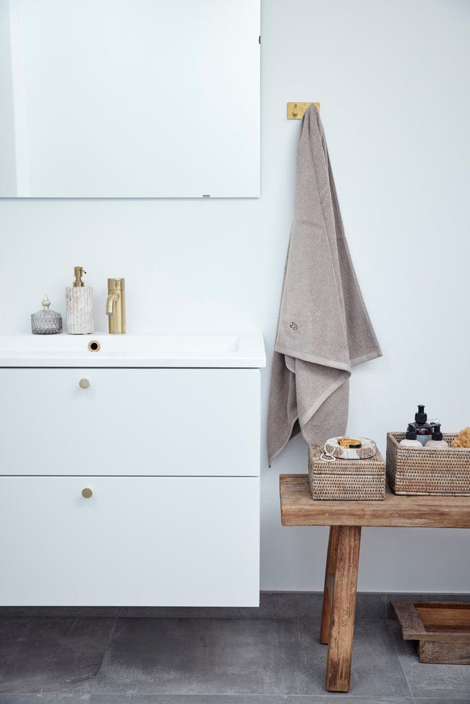 Handwoven rattan box on wooden bench in minimalist bathroom.