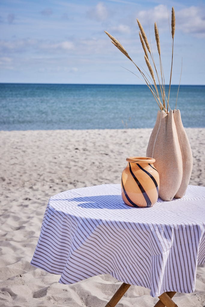 Olivia Tablecloth Ø140 cm Sand Striped on seaside table with decorative vases.