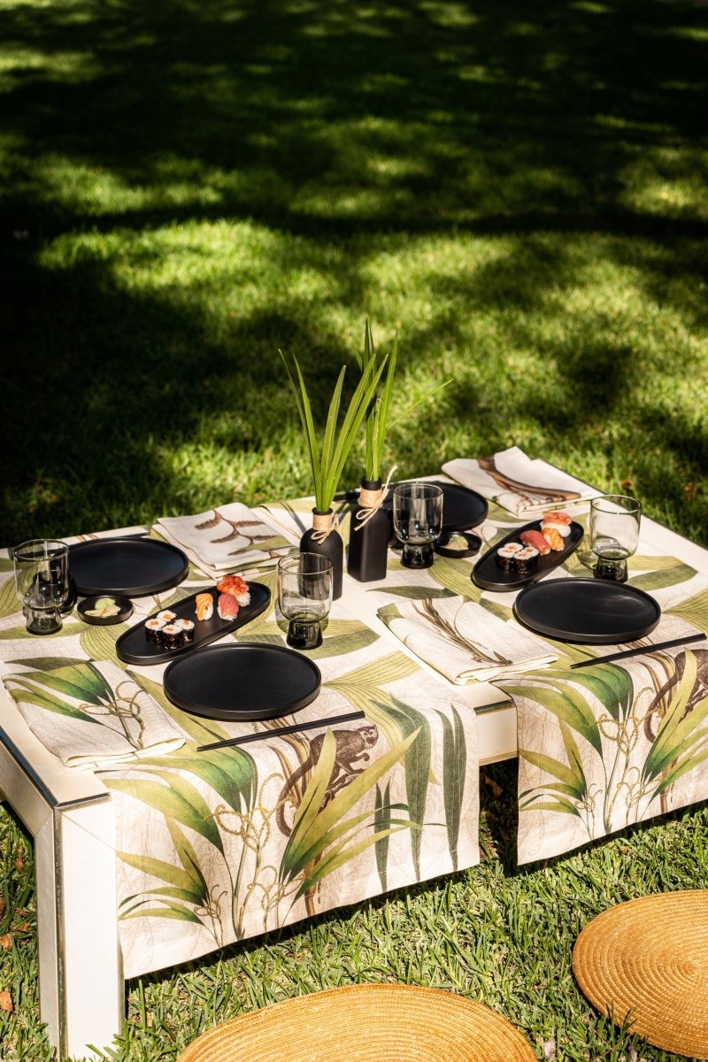 Dining table set with plates, glasses, and food on a grassy outdoor setting