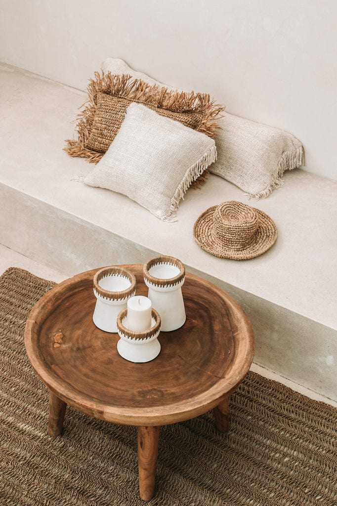 Pretty candle holder in white terracotta with raffia accent on a wooden table.