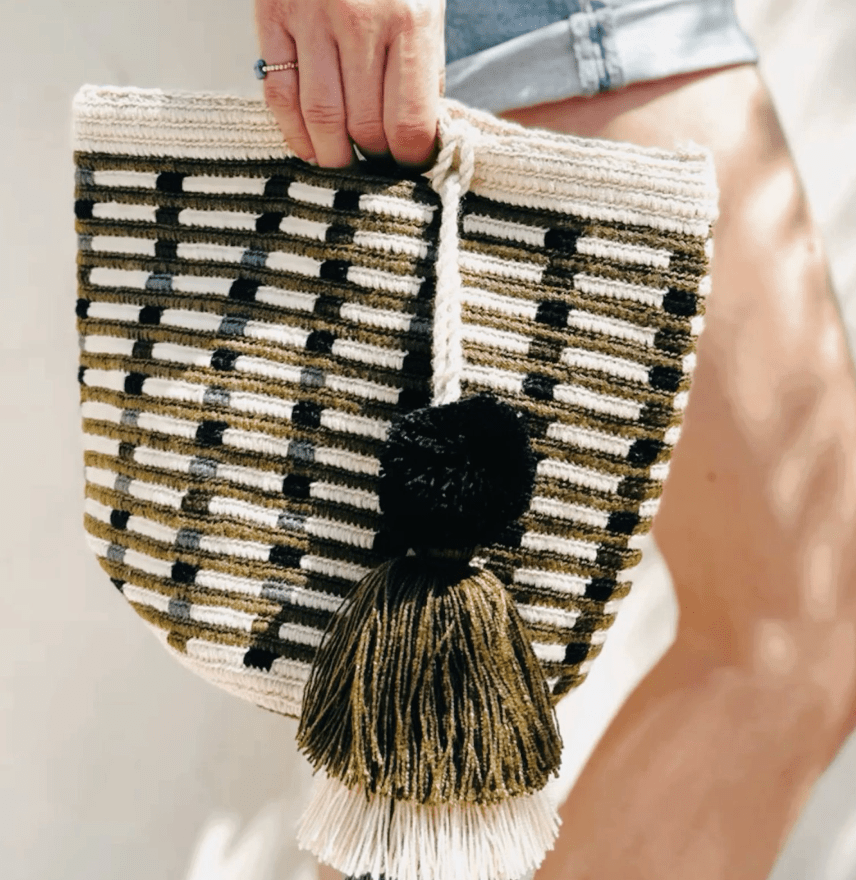 Woven clutch bag with black and white pattern and tassel held by a person.