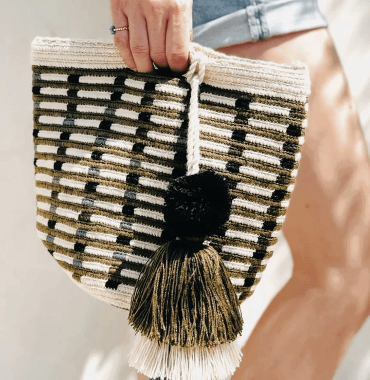 Woven clutch bag with black and white pattern and tassel held by a person.